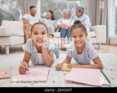 Deux jolies sœurs frères et sœurs de race mixte dessinant et colorant dans la salle de séjour avec leurs parents et grands-parents en arrière-plan. Enfants insouciants Banque D'Images