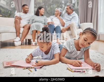Deux jolies sœurs frères et sœurs de race mixte dessinant et colorant dans la salle de séjour avec leurs parents et grands-parents en arrière-plan. Enfants insouciants Banque D'Images