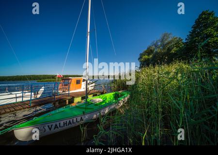 Jezioro Ostrowieckie, Pologne - juillet 2020 : Une petite jetée et des bateaux privés sur la rive d'un lac entouré de roseaux et d'arbres sous le ciel bleu Banque D'Images