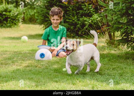 Joyeux garçon et chien jouant avec le trow automatique et la machine de fetch lancer des balles de tennis Banque D'Images