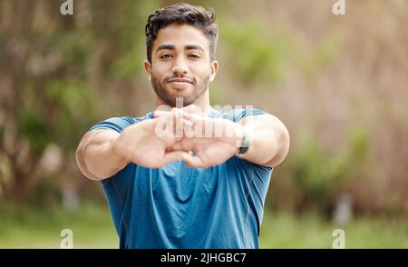 Portrait d'un jeune indien en forme étirant les bras pour l'échauffement afin d'éviter les blessures lors de l'exercice à l'extérieur. Athlète masculin préparant le corps et les muscles Banque D'Images