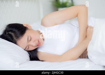 Jeune femme asiatique couché sur le lit douleur estomac ou intestin avec la maladie constipation ou indigestion dans la chambre à la maison, malheureuse femme malade et menstrua Banque D'Images
