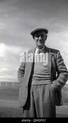 1950s, historique, debout dans sa veste et cravate et casquette en tissu, professionnel écossais de golf et clubmaker de golf, Tom Reekie d'Elie Golf Club, Fife, Écosse, Royaume-Uni. Né à St.Monans en 1880, Tom a fait un apprentissage et travaille avec le créateur de club de golf George Forrester à Earlsferry en 1895, y travaillant jusqu'à ce qu'il ait vu le service en WW1. Survivant à la guerre, en 1919, il a créé sa propre entreprise comme professionnel de golf et créateur de club à Elie et en 1946, il est devenu Tom Reekie & son, quand son fils John l'a rejoint. Banque D'Images