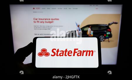 Personne tenant un smartphone avec le logo de State Farm Mutual automobile Insurance Company à l'écran devant le site Web. Mise au point sur l'affichage du téléphone. Banque D'Images