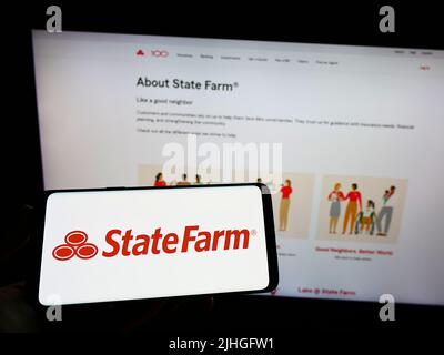 Personne tenant un téléphone portable avec le logo de State Farm Mutual automobile Insurance Company à l'écran en face de la page Web. Mise au point sur l'affichage du téléphone. Banque D'Images