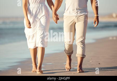 Gros plan de la course mixte jeune couple tenant les mains tout en marchant sur la plage ensemble. Couple hispanique voyageant et appréciant les vacances et l'être Banque D'Images