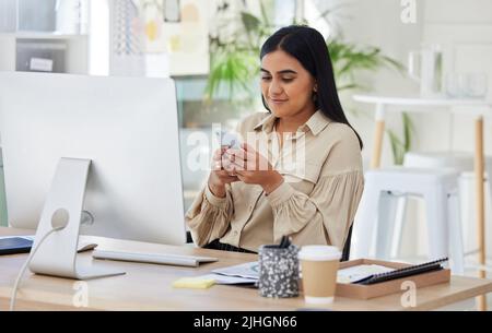 Une belle jeune femme d'affaires mixte de course utilisant son smartphone pendant une pause déjeuner au bureau au travail. Femme confiante et prospère Banque D'Images