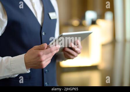 Une tablette numérique entre les mains d'un jeune réceptionniste d'un hôtel moderne de luxe, debout dans le salon à l'entrée et pour rencontrer de nouveaux clients Banque D'Images