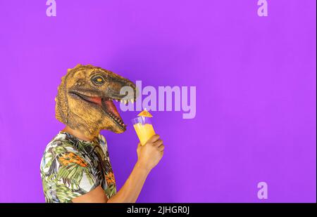 Homme portant un dinosaure masque de tête d'animal buvant un cocktail ou du jus de fruits isolés sur fond vert. Banque D'Images