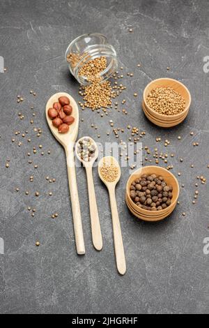 Graines de coriandre et allépice dans un pot en verre et des bols en bois. Noix et graines d'épices en cuillères. Les graines de coriandre sont dispersées sur la table. Pose à plat. Ba noir Banque D'Images