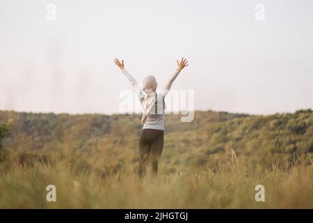 La jeune femme arabe pratique le yoga dans le parc d'été. Une femme musulmane regarde de côté faire de l'exercice en plein air et respirer de l'air frais en dehors des bras . FIT femme arabe formation dans un parc Banque D'Images