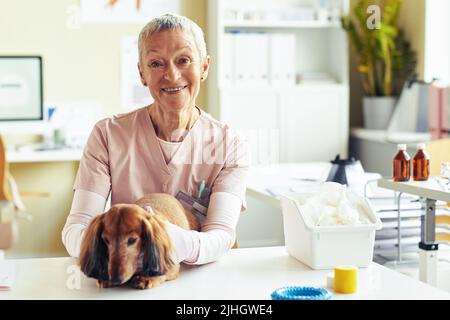 Portrait d'une femme âgée comme vétérinaire posant avec un petit chien dans une clinique vétérinaire et souriant à l'appareil photo, copier l'espace Banque D'Images