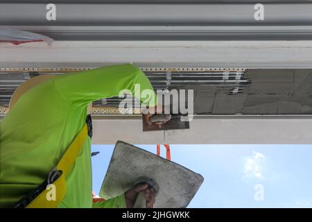 Ouvrier de construction sur un harnais, appliquant de la boue de stuc au dessus de la tête de soffit d'un grand bâtiment multiplex à Naples, en Floride. Nouvelle construction de la flèche Banque D'Images