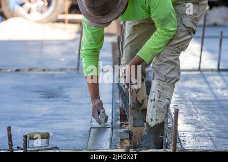 Un ouvrier de la construction utilise une truelle de virage pour terminer le bord d'une gifle de béton fraîchement versée comme une allée. Banque D'Images