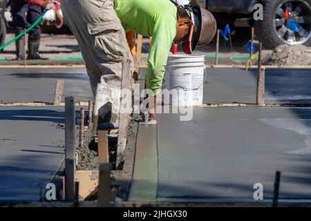 Un ouvrier de la construction utilise une truelle de virage pour terminer le bord d'une gifle de béton fraîchement versée comme une allée. Banque D'Images