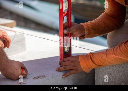 Deux ouvriers de la construction, maçons, utilisant un niveau pour marquer et mesurer à partir d'une ligne rouge sbronzée avant Banque D'Images