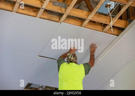 Le poste de cloisons sèches de construction qualifiée installe un panneau de cloisons sèches sur mesure au plafond d'une habitation. Nouvelle construction Banque D'Images