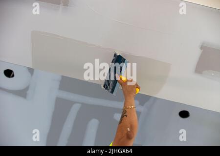 travailleur de la construction qualifié appliquant du plâtre blanc sur une poutre de plafond dans une habitation résidentielle au cours de la nouvelle construction. Banque D'Images