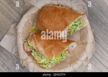 Vue en hauteur d'un sandwich au jambon chargé avec du fromage provolone, de la tomate, du mayonnaise et de l'oignon rouge à l'intérieur d'un rouleau italien pour un repas de déjeuner copieux. Banque D'Images