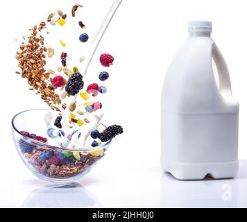 Granola volante dans un bol en verre. Les baies, le lait et le granola tombent dans une assiette. Lait et granola. Lévitation de baies et de lait. Isoler. Banque D'Images