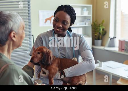Portrait de jeune vétérinaire souriant tenant chien mignon dans la clinique vétérinaire et client de consultation Banque D'Images