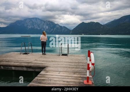 Attersee - célèbre lac turquoise autrichien. La vue sur la femme qui se tient sur la jetée en bois qui regarde le lac et de belles montagnes nuageux dans le Banque D'Images