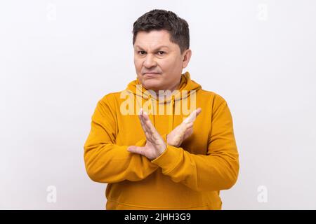 Non, absolument pas. Portrait de l'homme d'âge moyen montrant x signe avec les mains croisées, ce qui signifie arrêt, c'est la fin, portant le sweat à capuche de style urbain. Studio d'intérieur isolé sur fond blanc. Banque D'Images