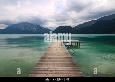 Attersee - célèbre lac turquoise autrichien. La vue sur la longue jetée en bois et les montagnes en arrière-plan. Ciel nuageux. Banque D'Images