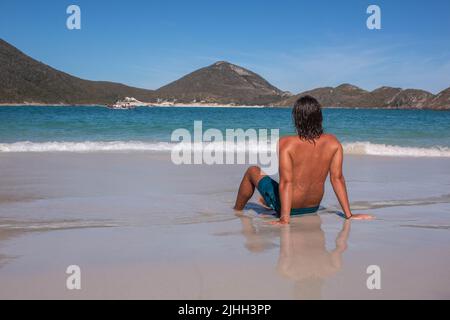 Jeune homme assis sur le sable sur les plages paradisiaques de Pontal do Atalaia, Cabo Frio, Brésil. Banque D'Images