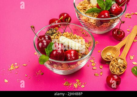 Concept petit déjeuner été. Une nourriture saine le matin. Cerises mûres, lait, chocolat blanc et granola. Arrière-plan rose, plat, espace de copie Banque D'Images