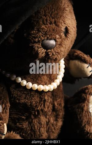 Un ours en peluche brun de la 1980s vêtu d'un grand chapeau de femme et d'un collier de perles. Banque D'Images