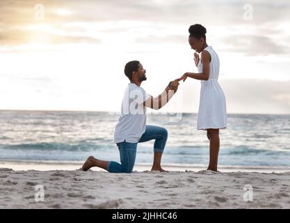 Petit ami demandant à sa petite amie de l'épouser tout en se tenant sur la plage ensemble. Homme afro-américain proposant à sa petite amie par le bord de mer Banque D'Images