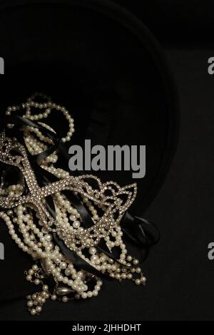 Un tas de colliers de perles de près et sur un fond neutre avec des accessoires comme un vase, un vieux chapeau, un masque, et des canisters de stockage rouge/or. Banque D'Images