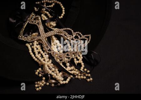 Un tas de colliers de perles de près et sur un fond neutre avec des accessoires comme un vase, un vieux chapeau, un masque, et des canisters de stockage rouge/or. Banque D'Images