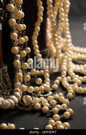 Un tas de colliers de perles de près et sur un fond neutre avec des accessoires comme un vase, un vieux chapeau, un masque, et des canisters de stockage rouge/or. Banque D'Images