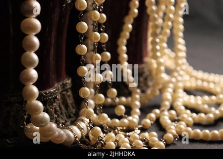 Un tas de colliers de perles de près et sur un fond neutre avec des accessoires comme un vase, un vieux chapeau, un masque, et des canisters de stockage rouge/or. Banque D'Images