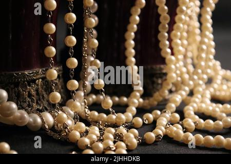 Un tas de colliers de perles de près et sur un fond neutre avec des accessoires comme un vase, un vieux chapeau, un masque, et des canisters de stockage rouge/or. Banque D'Images