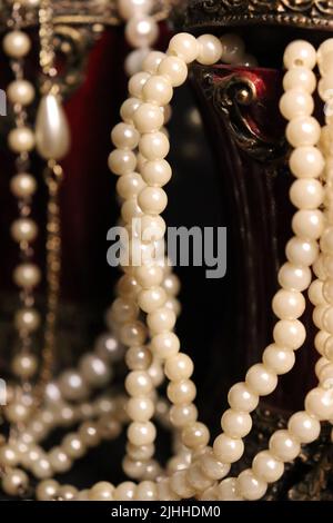 Un tas de colliers de perles de près et sur un fond neutre avec des accessoires comme un vase, un vieux chapeau, un masque, et des canisters de stockage rouge/or. Banque D'Images