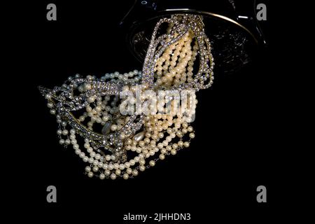 Un tas de colliers de perles de près et sur un fond neutre avec des accessoires comme un vase, un vieux chapeau, un masque, et des canisters de stockage rouge/or. Banque D'Images