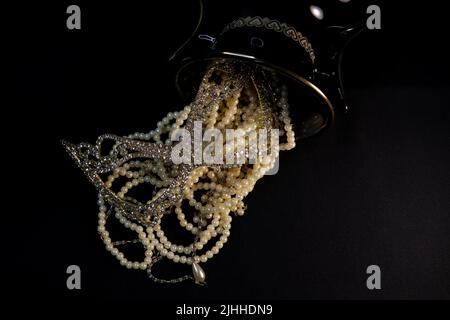 Un tas de colliers de perles de près et sur un fond neutre avec des accessoires comme un vase, un vieux chapeau, un masque, et des canisters de stockage rouge/or. Banque D'Images