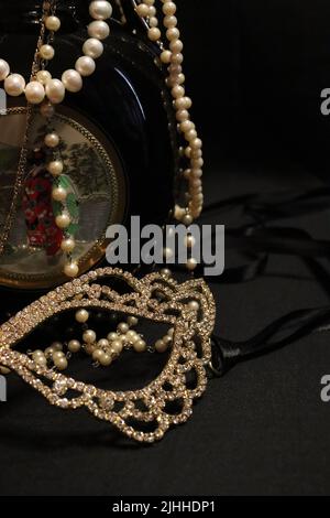 Un tas de colliers de perles de près et sur un fond neutre avec des accessoires comme un vase, un vieux chapeau, un masque, et des canisters de stockage rouge/or. Banque D'Images