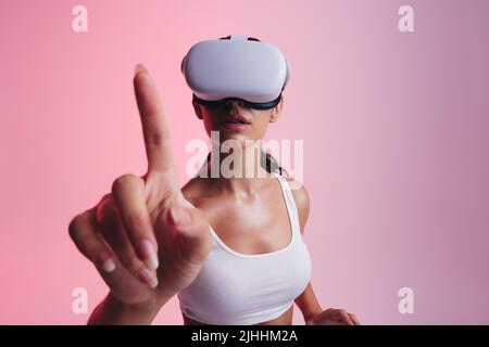 Femme en interaction avec la réalité virtuelle dans un studio. Jeune femme utilisant son doigt pour toucher l'espace virtuel tout en portant un casque de réalité virtuelle. Femme Banque D'Images