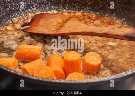 Les carottes sont frites dans une casserole sur un poêle à gaz pour faire du poisson cuit avec des champignons et des pommes de terre Banque D'Images