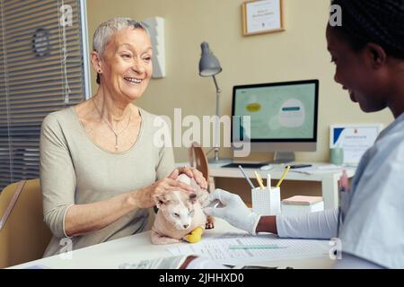Portrait d'une femme âgée souriante tenant un chat à la clinique vétérinaire et consultant avec une jeune femme vétérinaire Banque D'Images
