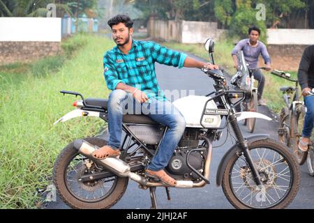 Un jeune indien qui fait une moto près d'un champ de paddy Banque D'Images