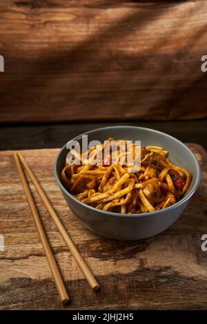 Bami Goreng, spécialité indonésienne de pâtes dans un bol en bois avec baguettes Banque D'Images