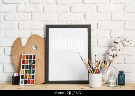 Cadre photo comme chevalet avec les outils de l'artiste sur une table en bois contre un mur en brique blanche Banque D'Images