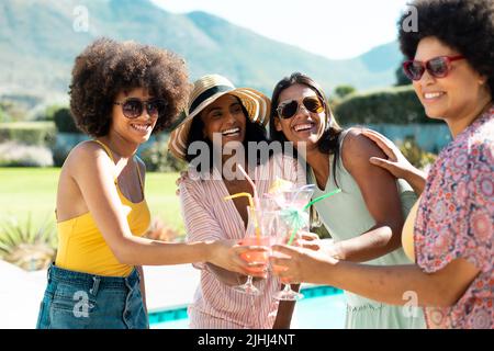 De jeunes amies biraciales se sont réjouie de déguster des cocktails tout en s'amusant à la fête au bord de la piscine en été Banque D'Images
