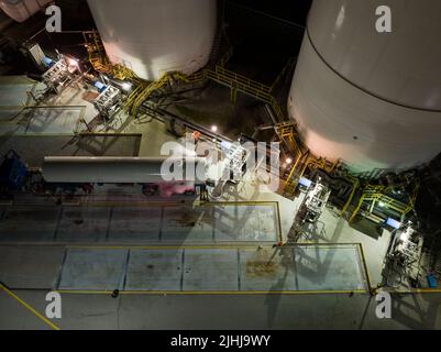 Une vue aérienne au-dessus d'une grande installation de gaz liquide comme un camion-citerne de transport est en train d'être rempli tard la nuit, sous des lumières vives. Banque D'Images