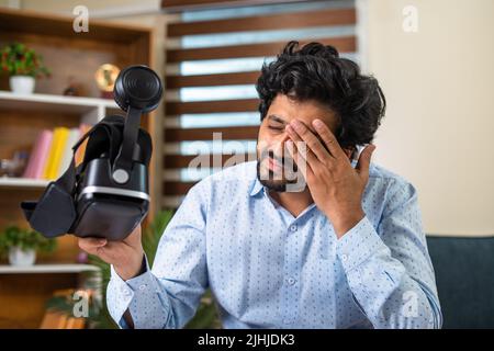 Un jeune homme se frottant les yeux après une utilisation intensive de VR ou de lunettes de réalité virtuelle au bureau pour la réunion - concept de technologie, métaverse et virtuel Banque D'Images